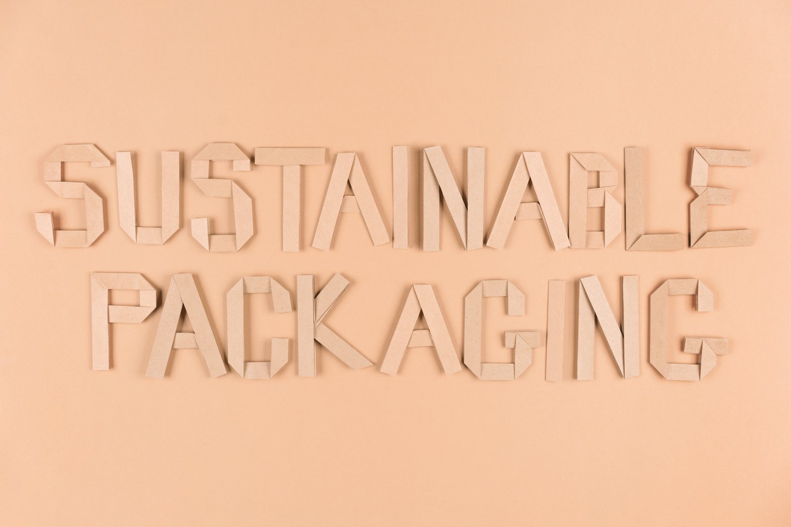 Sustainable paper packaging concept. Text Sustainable Packaging over light brown background. Flat lay style